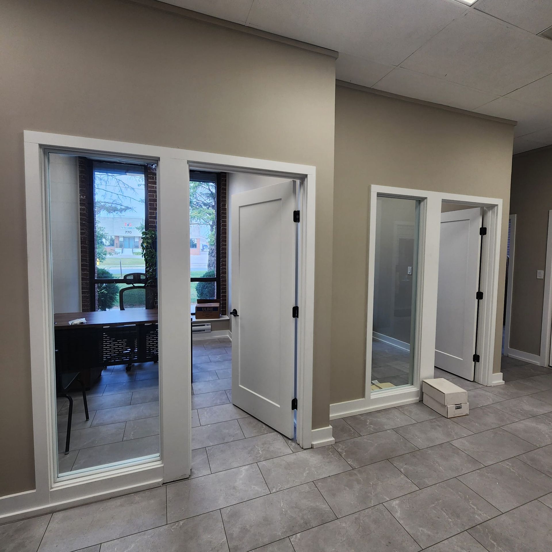 Interior view of an office space with three doorways and a large window. Neutral color walls and gray tile flooring.