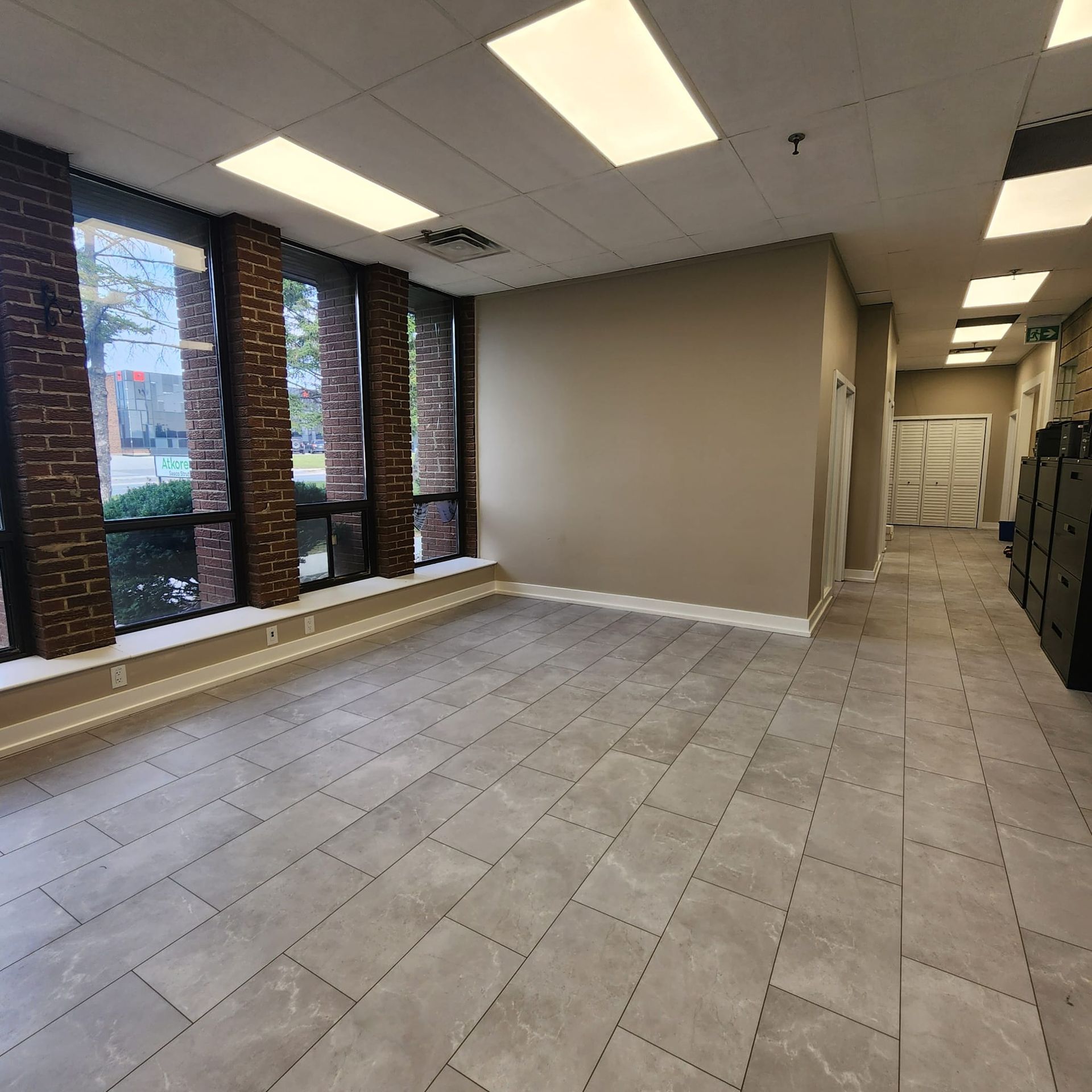 Empty interior room with gray tiled floor, large windows, and neutral walls.