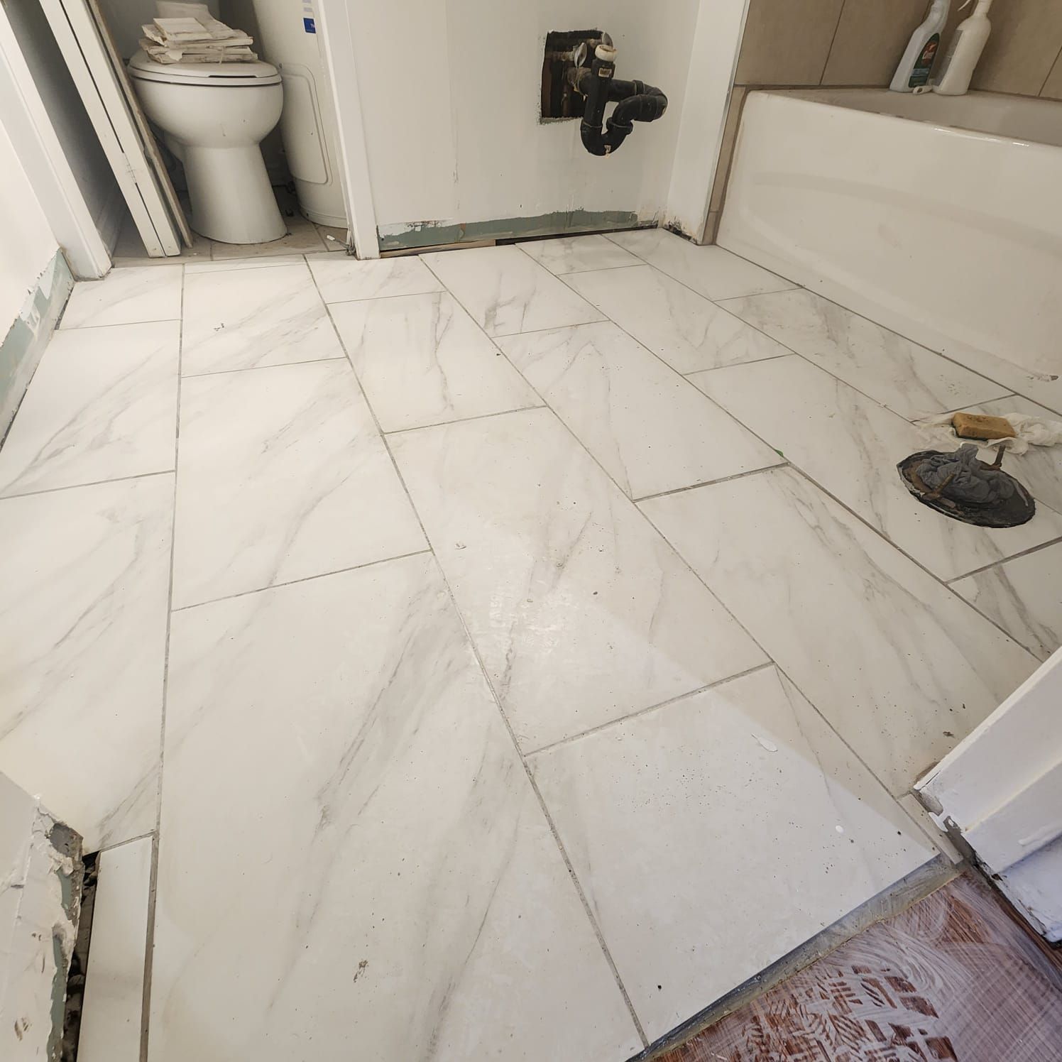 Bathroom floor tiled with large, rectangular, marble-like tiles. Toilet and tub are visible, undergoing renovation.