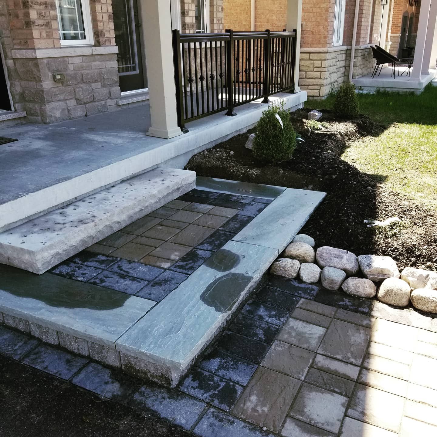 Stone steps and walkway leading to a house with black railing and small garden bed.