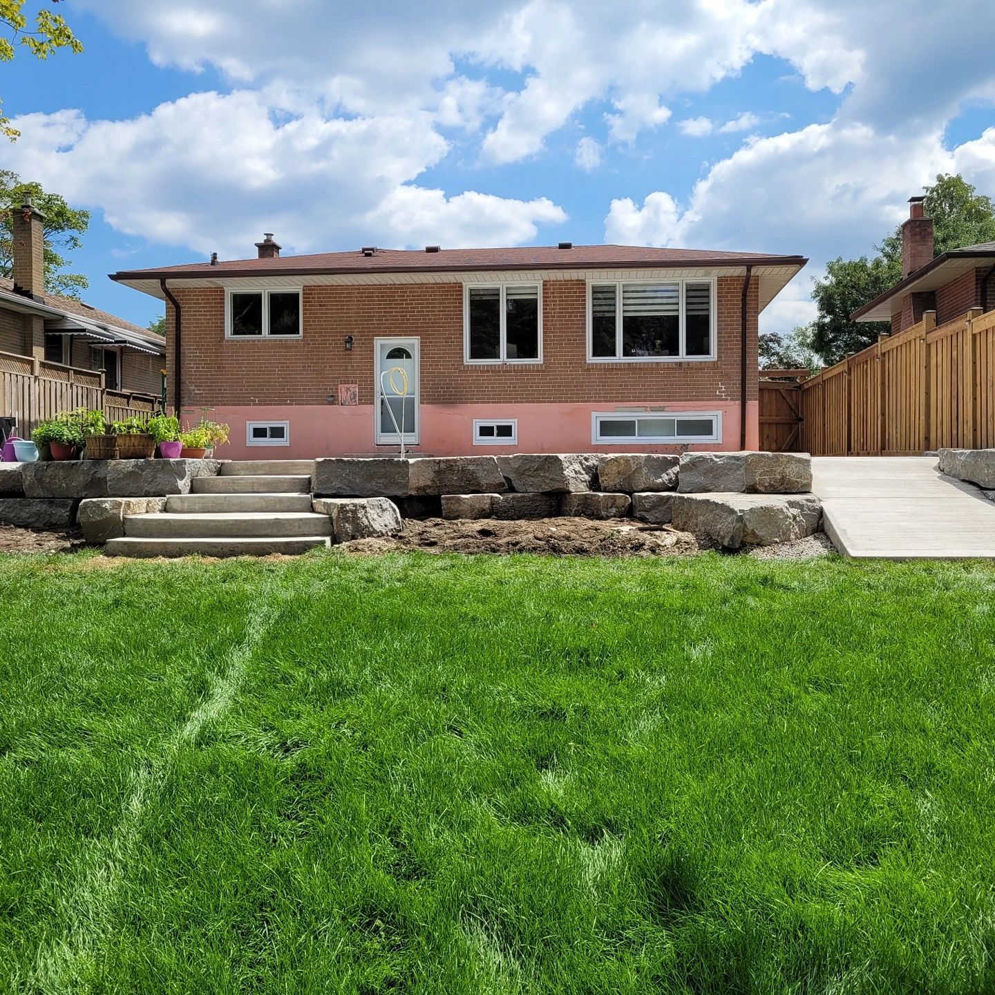 Backyard view of a house with stone steps, a concrete ramp, and a green lawn under a cloudy sky.