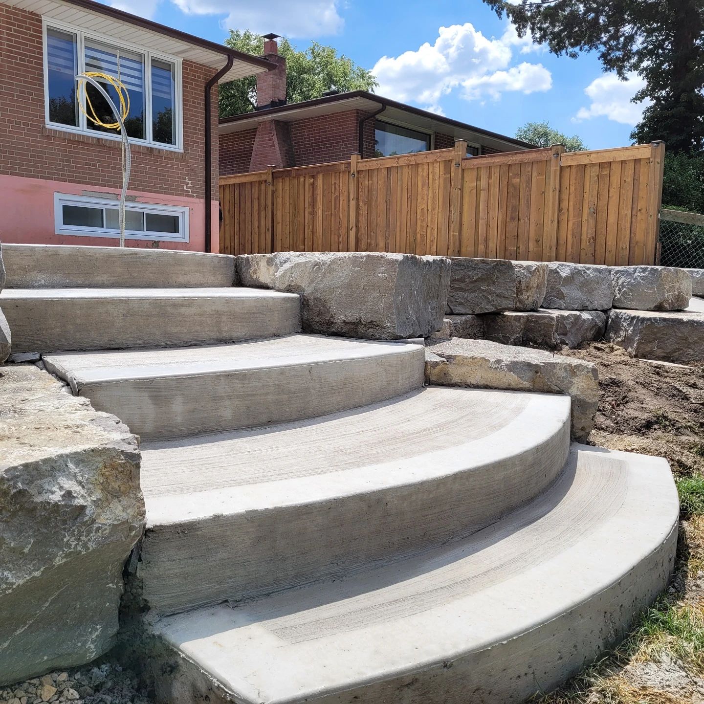 Concrete steps with curved edges and rock retaining wall, leading up to a wooden fence.