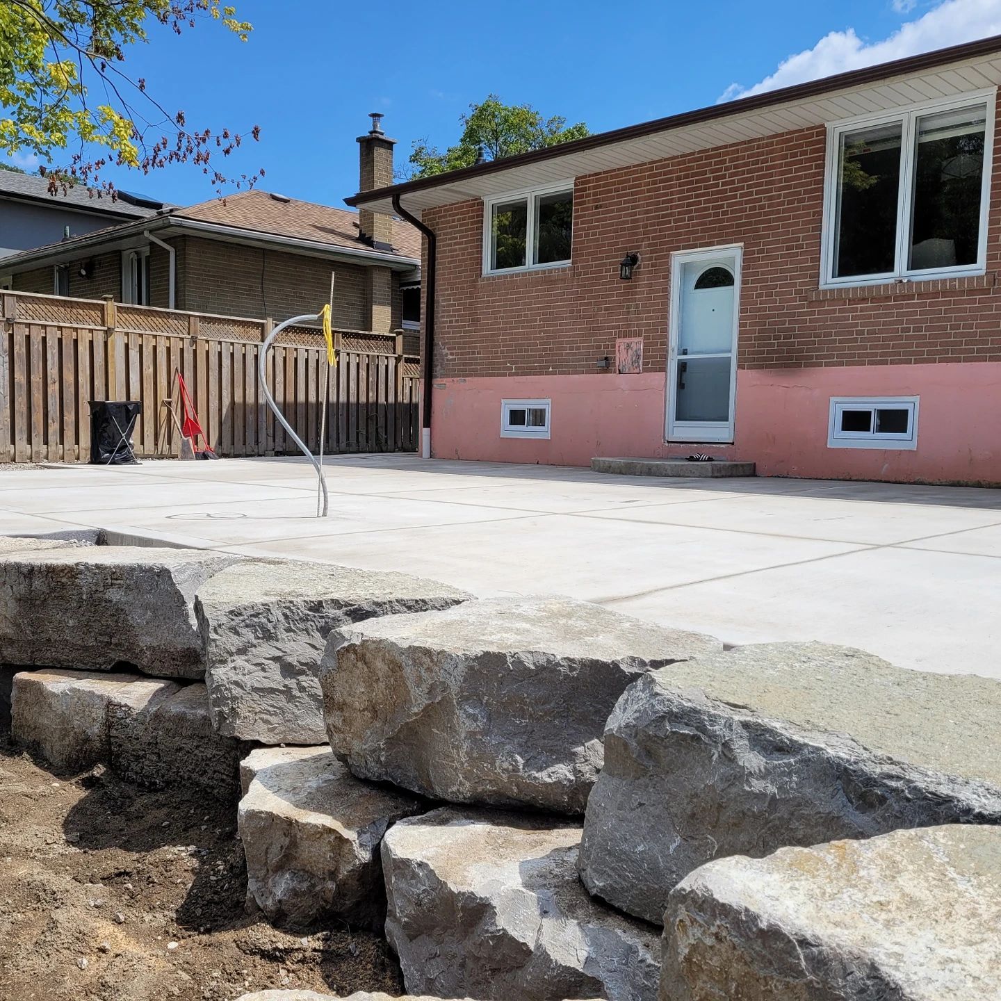 Backyard with a stacked stone retaining wall, concrete patio, and brick house with a door.