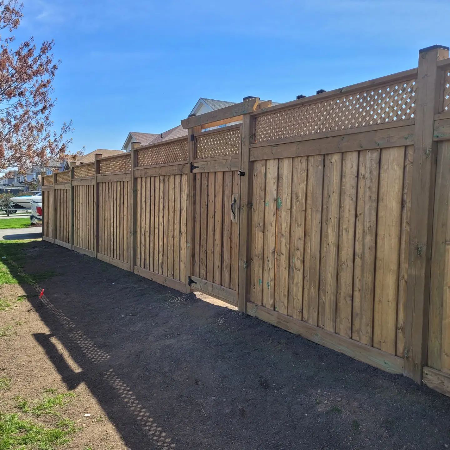 Wooden fence with gate, set against a blue sky, runs alongside a gravel path.