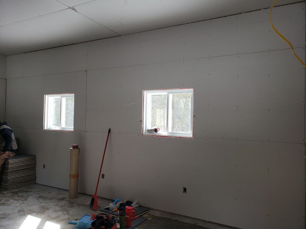 Interior view of a room under construction with drywall and two windows.