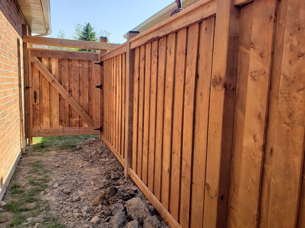 Wooden fence and gate with stained finish, set against a brick building and bare earth.