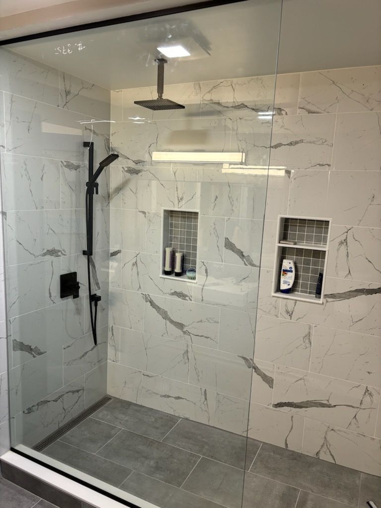Modern shower with marble-look tiles, glass enclosure, black fixtures, and built-in niches for toiletries.