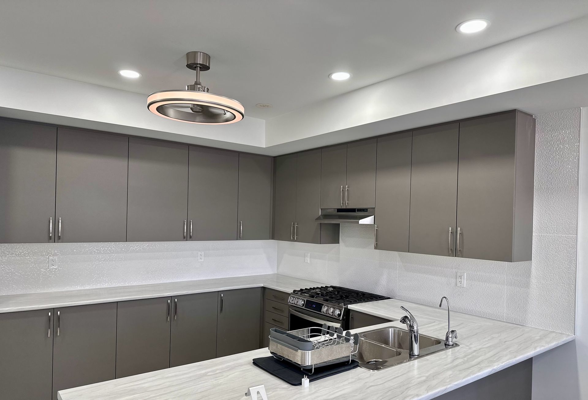 Modern gray kitchen with upper cabinets, countertops, and stainless steel appliances.