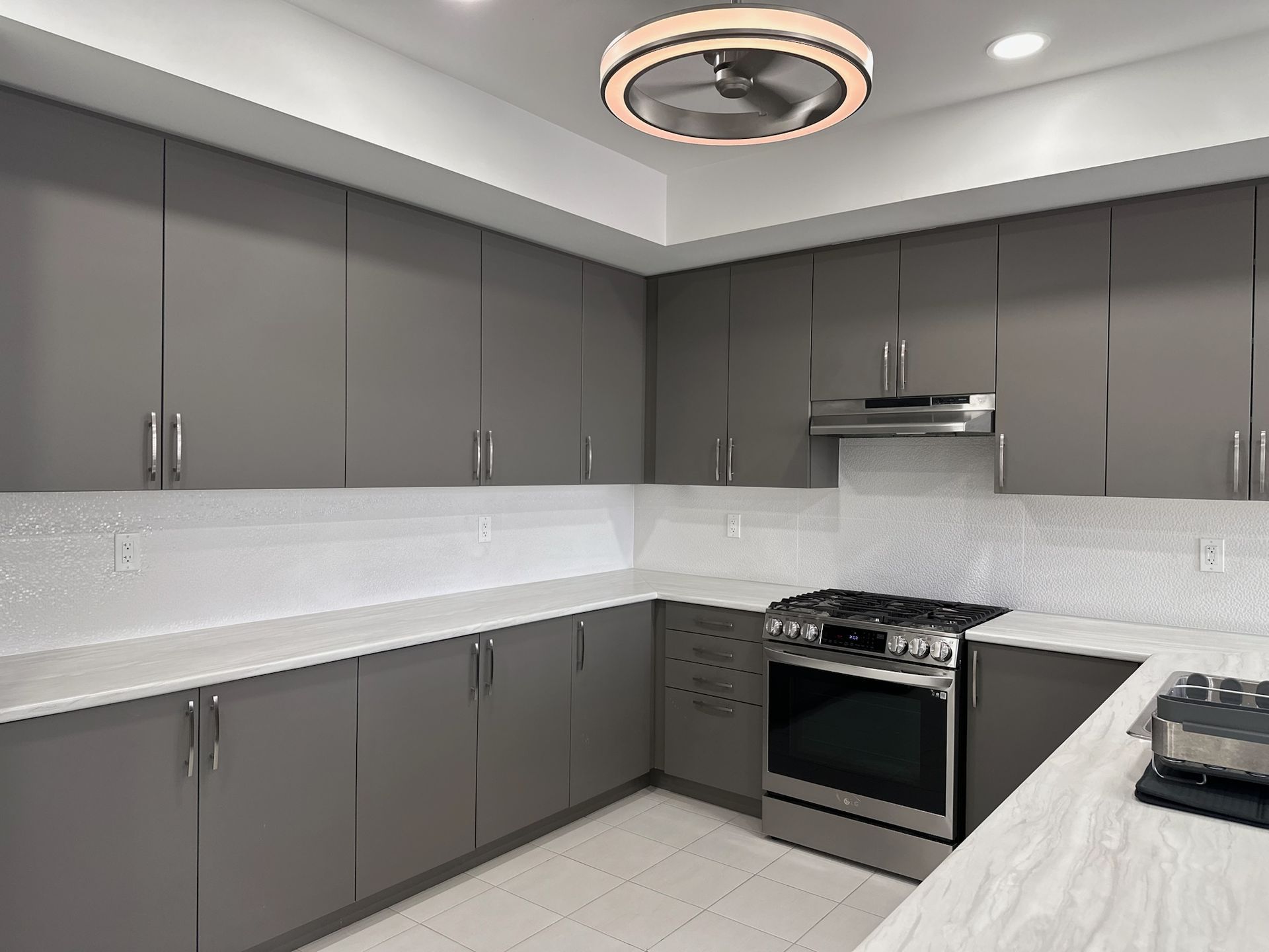 Modern gray kitchen with stainless steel appliances, white countertops, and white backsplash.