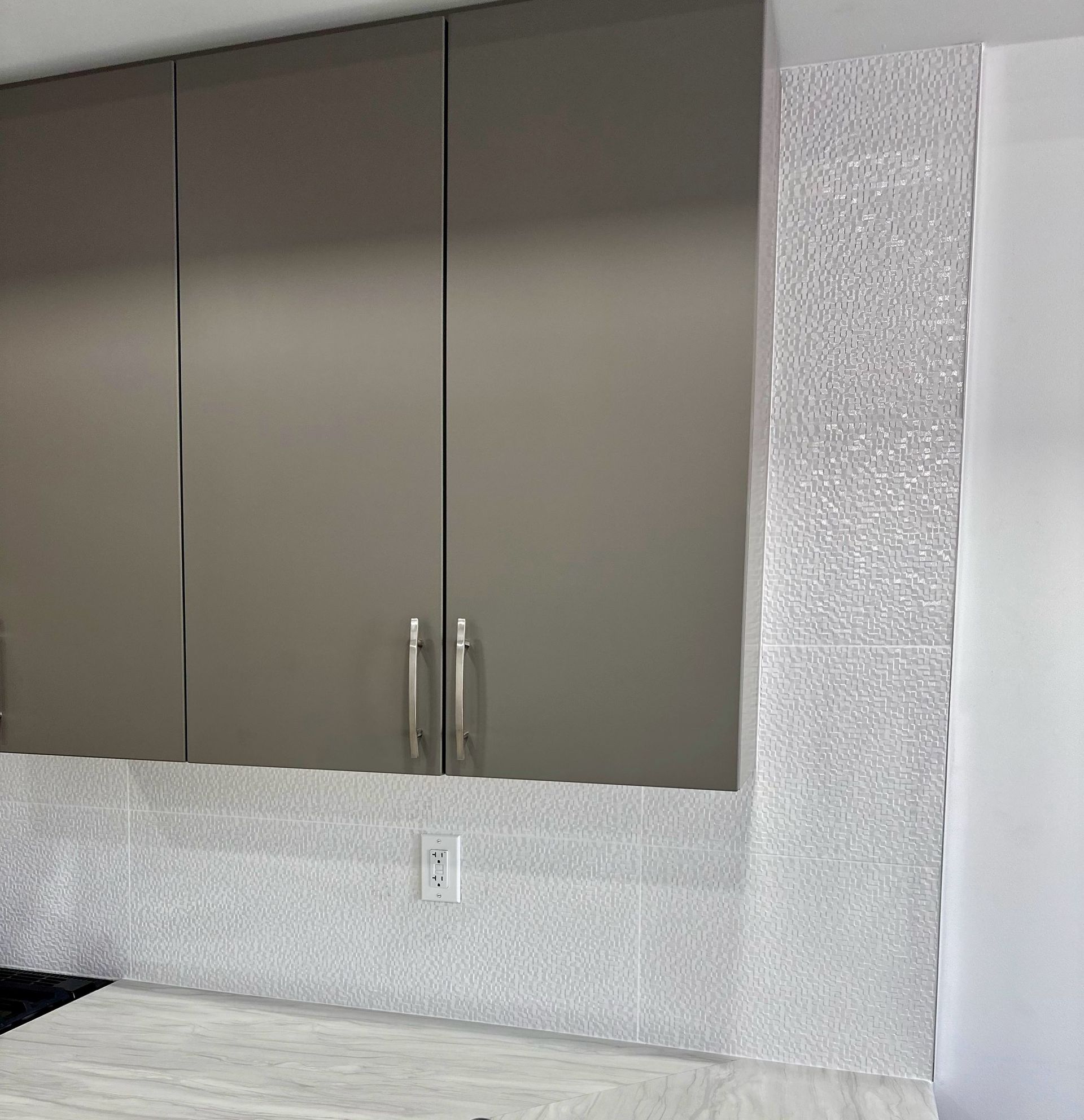 Gray kitchen cabinets with a textured white tile backsplash and countertop.