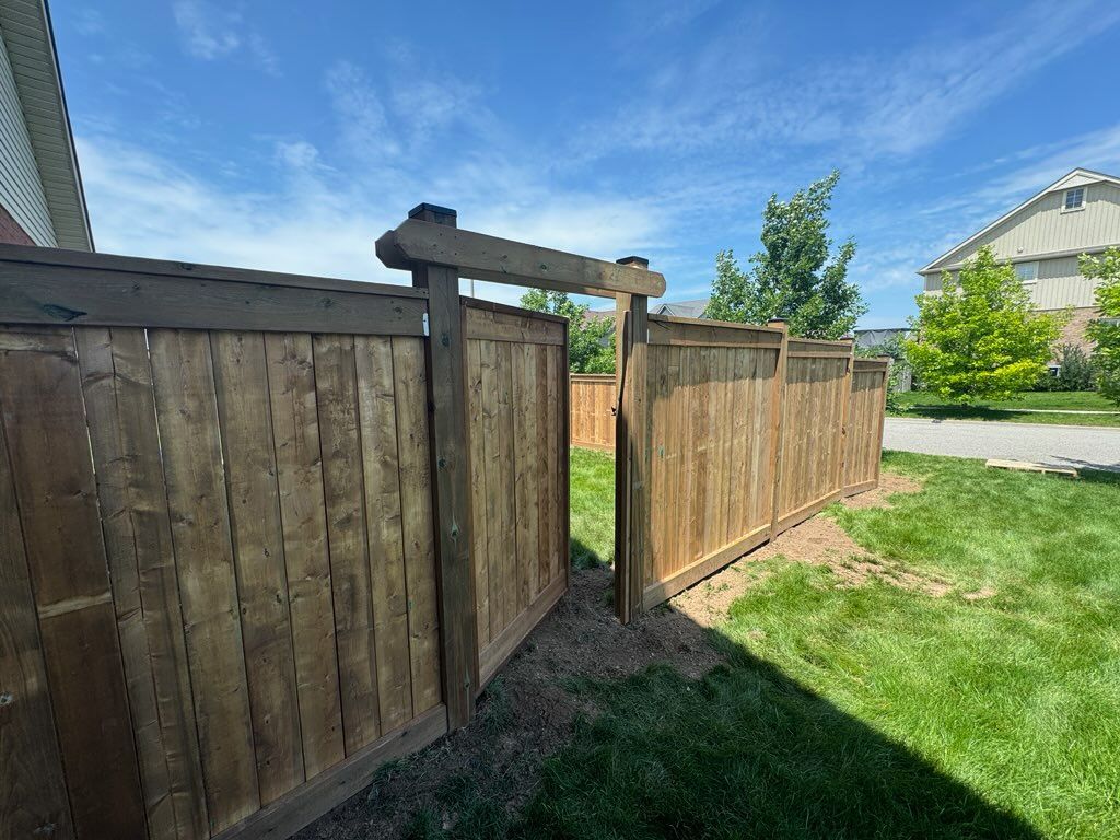 Wooden fence with a gate, in a backyard, under a blue sky.
