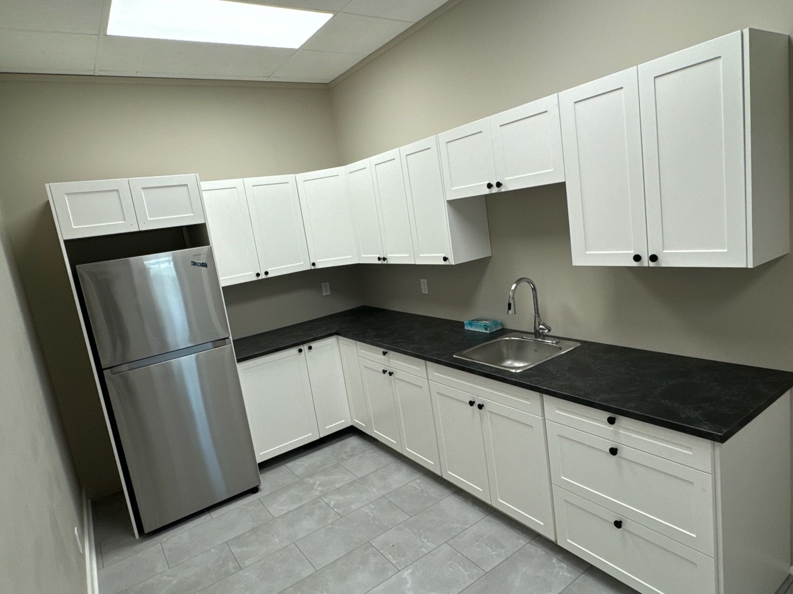 L-shaped white kitchen with black countertop, stainless steel refrigerator, and a sink.