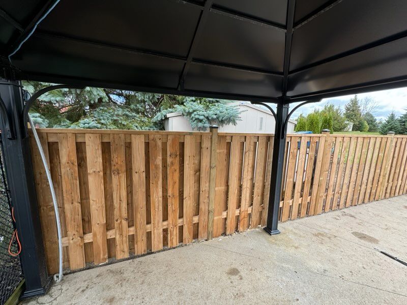 A wooden fence lines a patio area under a black gazebo.