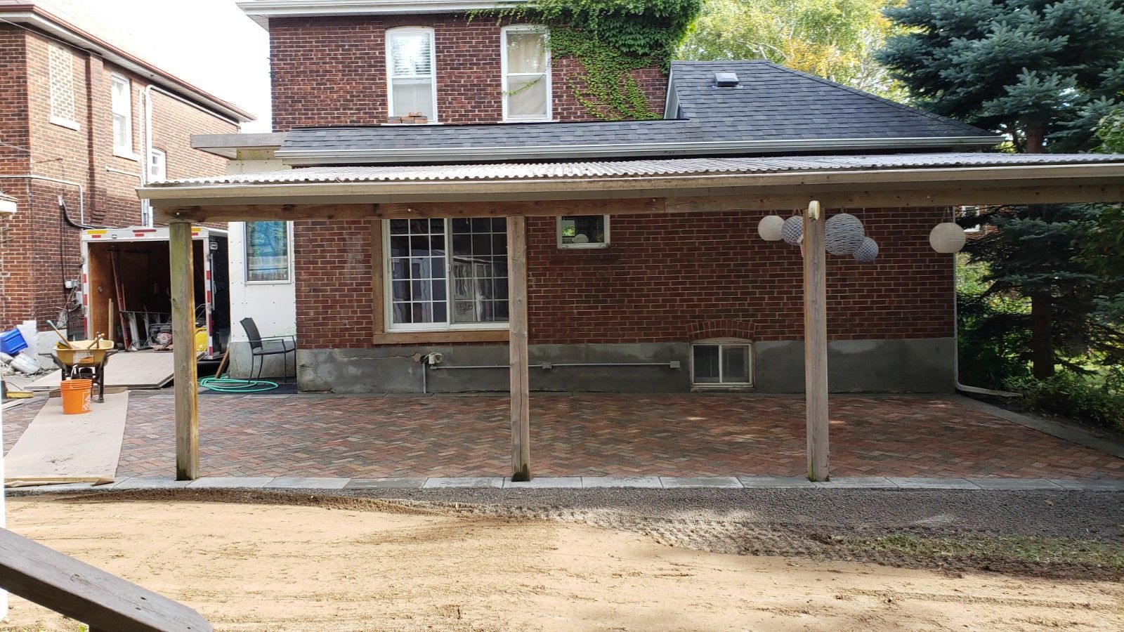 Brick house with a covered patio, brick pavers, wooden posts, and a gravel lawn.