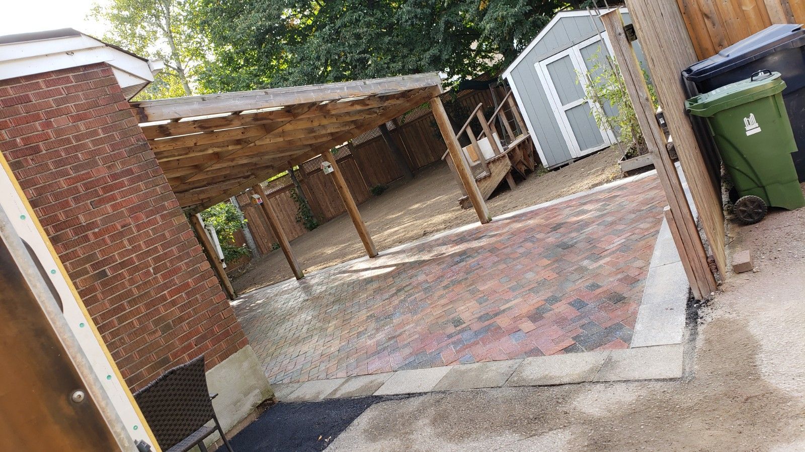 Brick patio with a wooden pergola, shed, and trash cans.