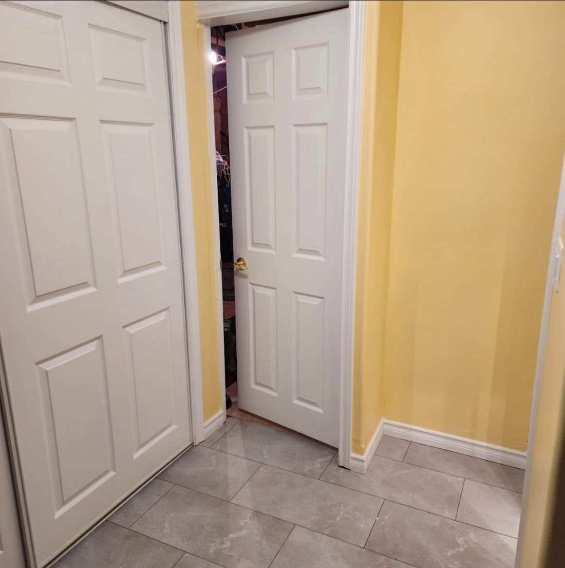White doors in a hallway with yellow walls and gray tiled floor; one door is open.