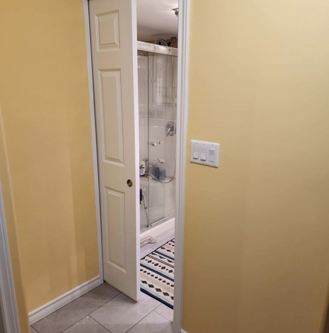 Yellow hallway with a partially open white door leading to a bathroom with a shower and rug.