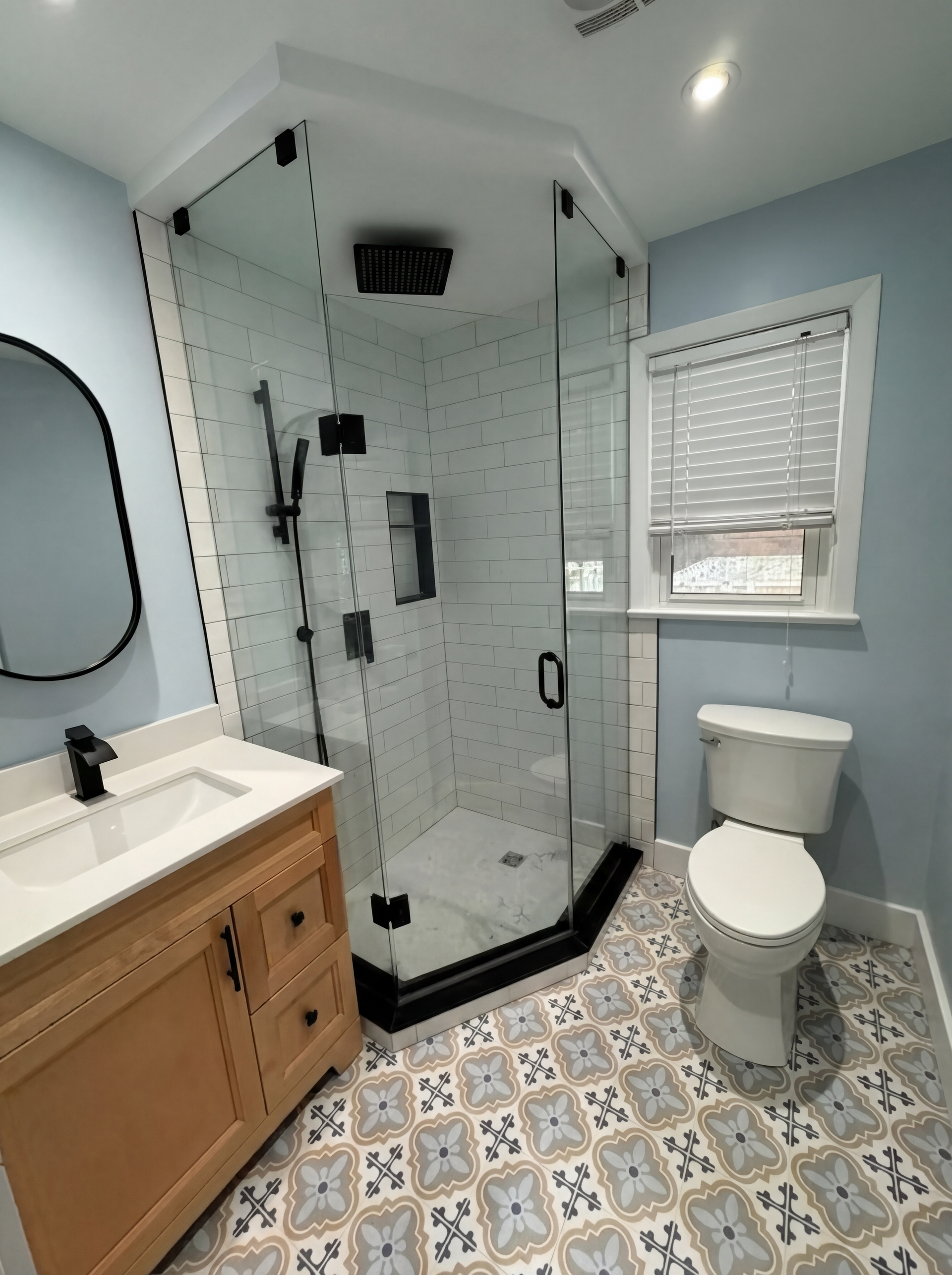 Bathroom with glass shower, patterned floor, wooden vanity, and blue walls.