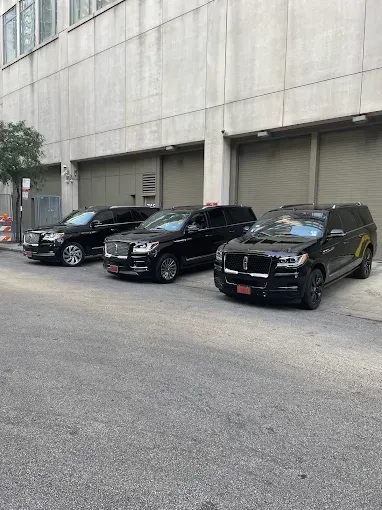 Three black SUVs parked in front of a tan building.