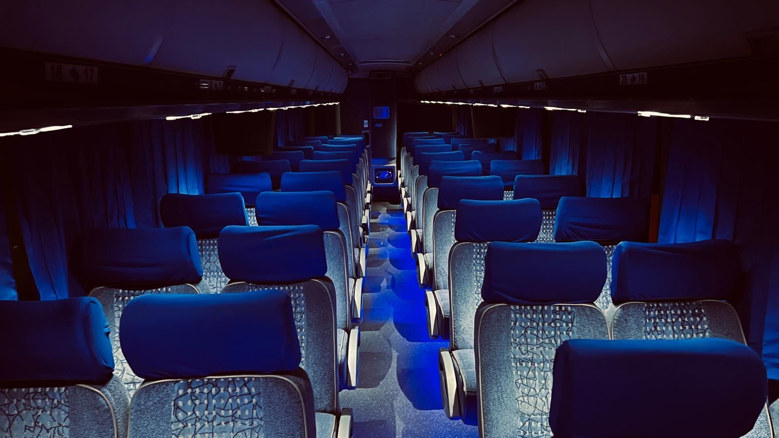 Dark interior of a bus with blue seats and ambient lighting, viewed down the aisle.