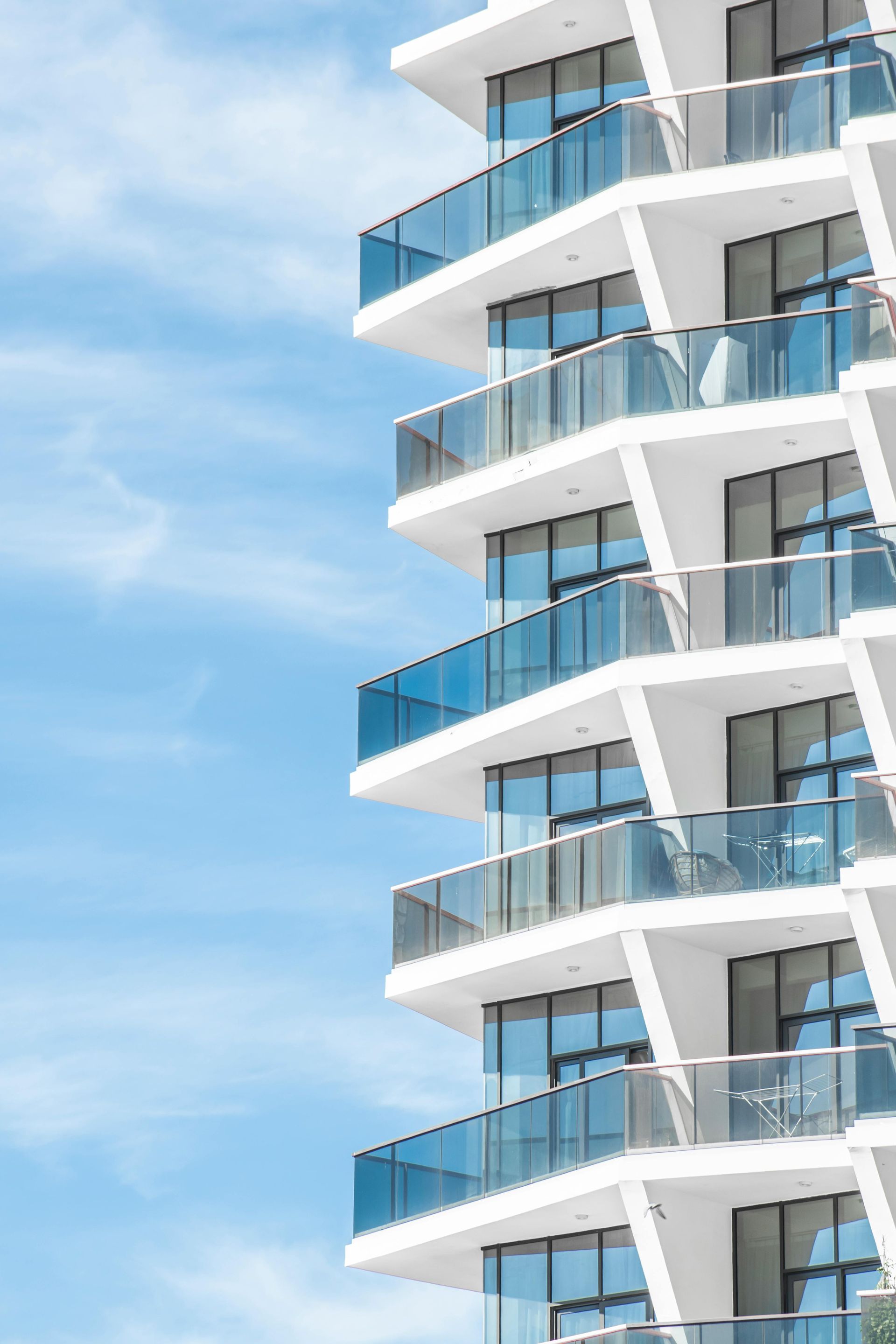Modern white building with angled balconies against a bright blue sky.