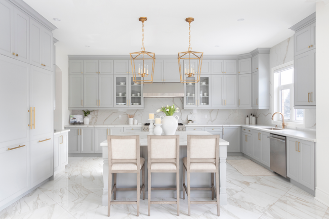 A kitchen with white cabinets and marble floors and a large island.