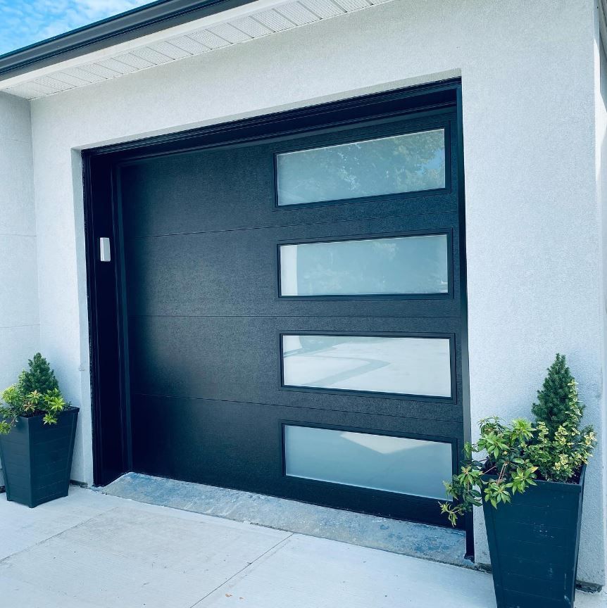 A black garage door with a few potted plants in front of it.