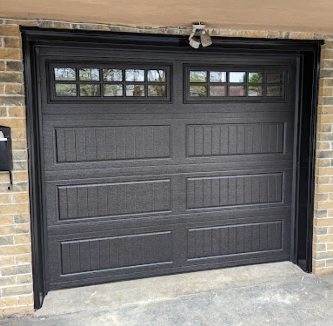 A black garage door with a brick wall behind it