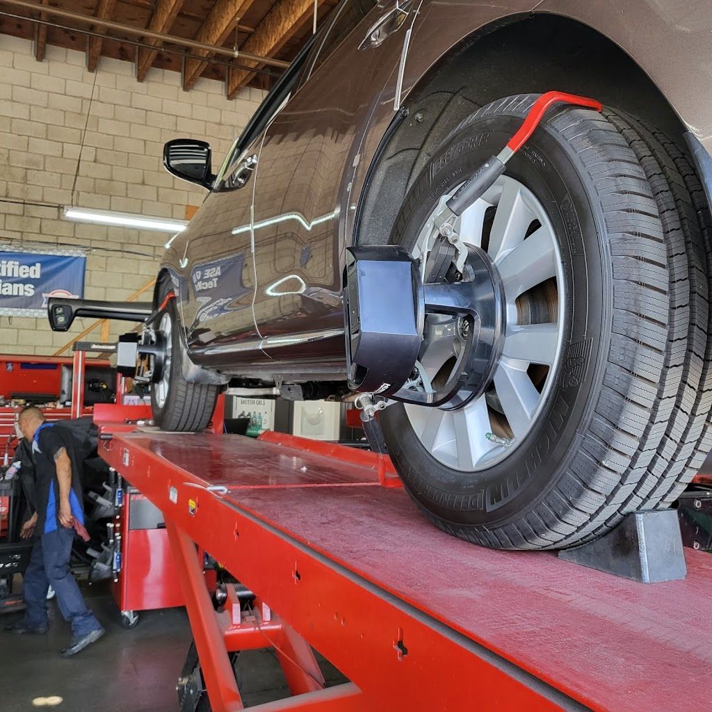 Car being aligned on a red lift in a garage; mechanic works on the front left wheel. | Nutech Auto Repair