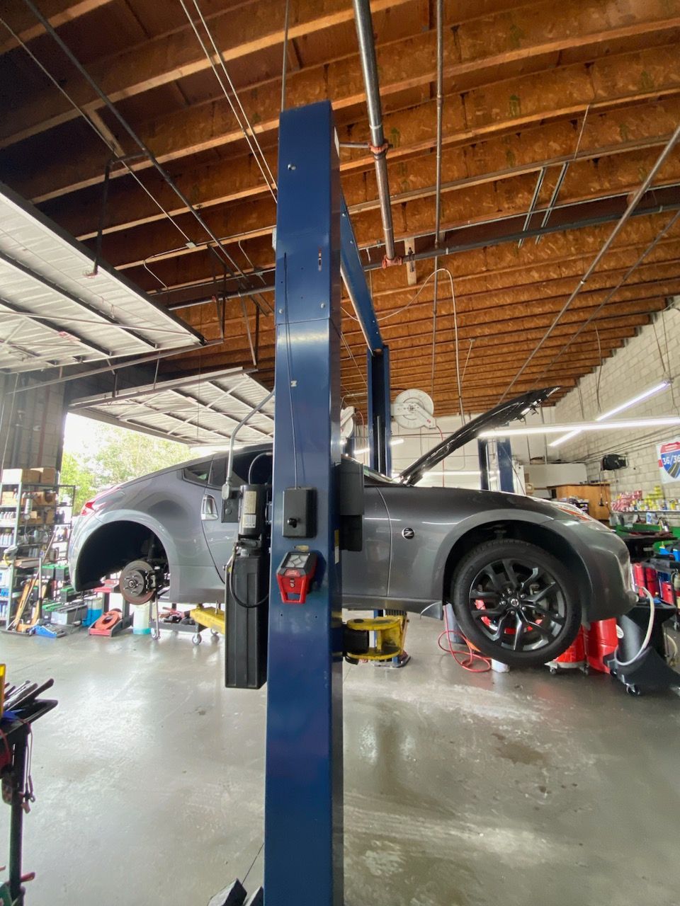 A gray car is on a lift inside a garage with tools, the hood open, and a mechanic is at work. | Nutech Auto Repair
