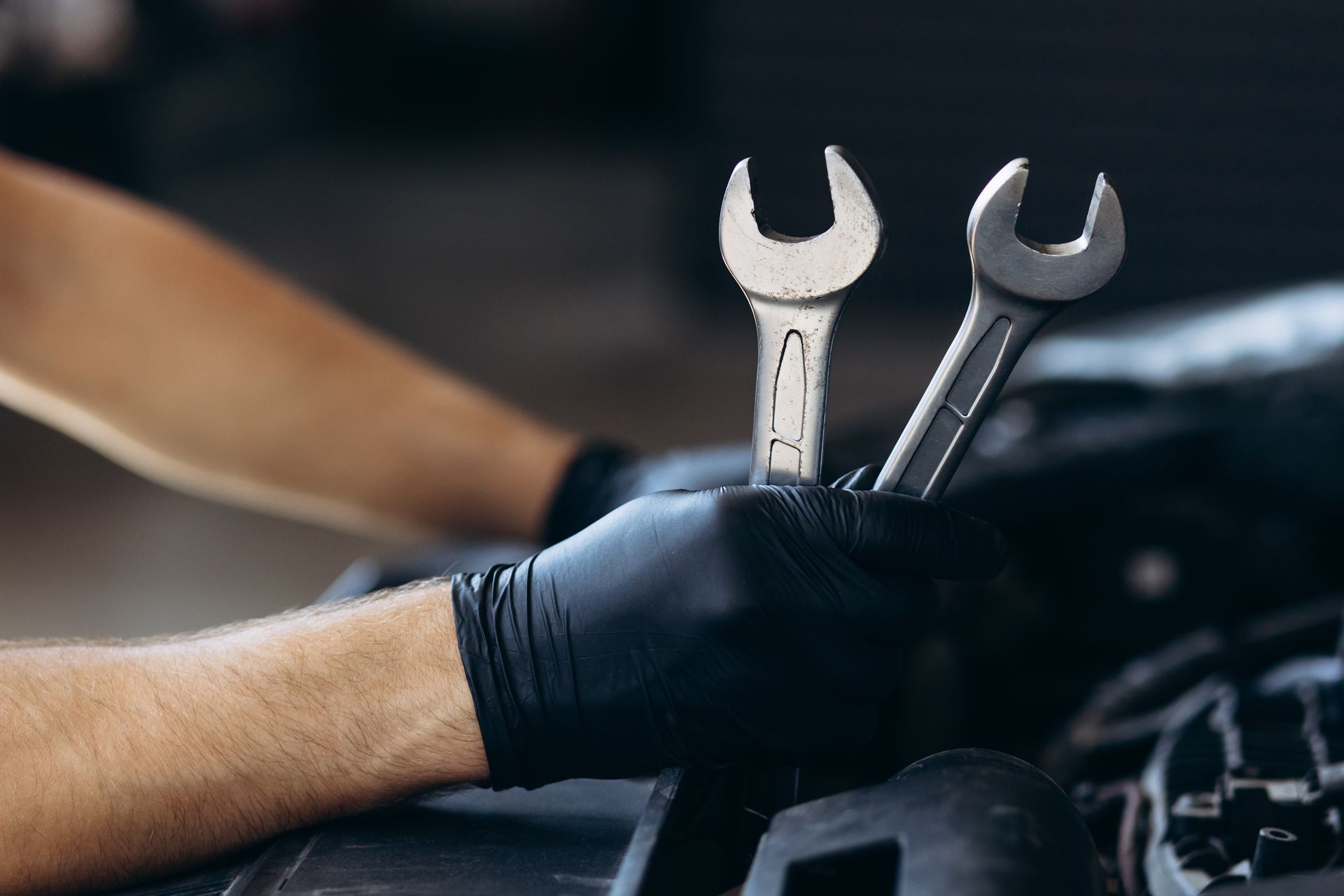 A mechanic wearing black gloves is holding two wrenches in his hands.
