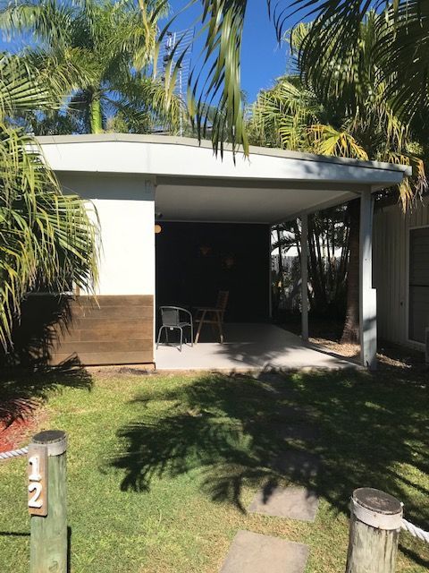 A Small House With A Porch And A Patio In The Middle Of A Lush Green Field Surrounded By Palm Trees — Bush Village Holiday Cabins In Cannonvale, QLD