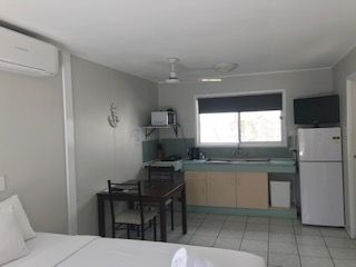 A Hotel Room With a Bed, Table, Chairs and Refrigerator — Bush Village Holiday Cabins In Cannonvale, QLD