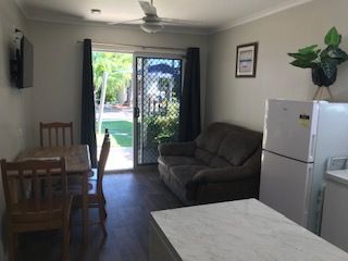 A Living Room With A Couch, Table, Chairs And A Refrigerator — Bush Village Holiday Cabins In Cannonvale, QLD