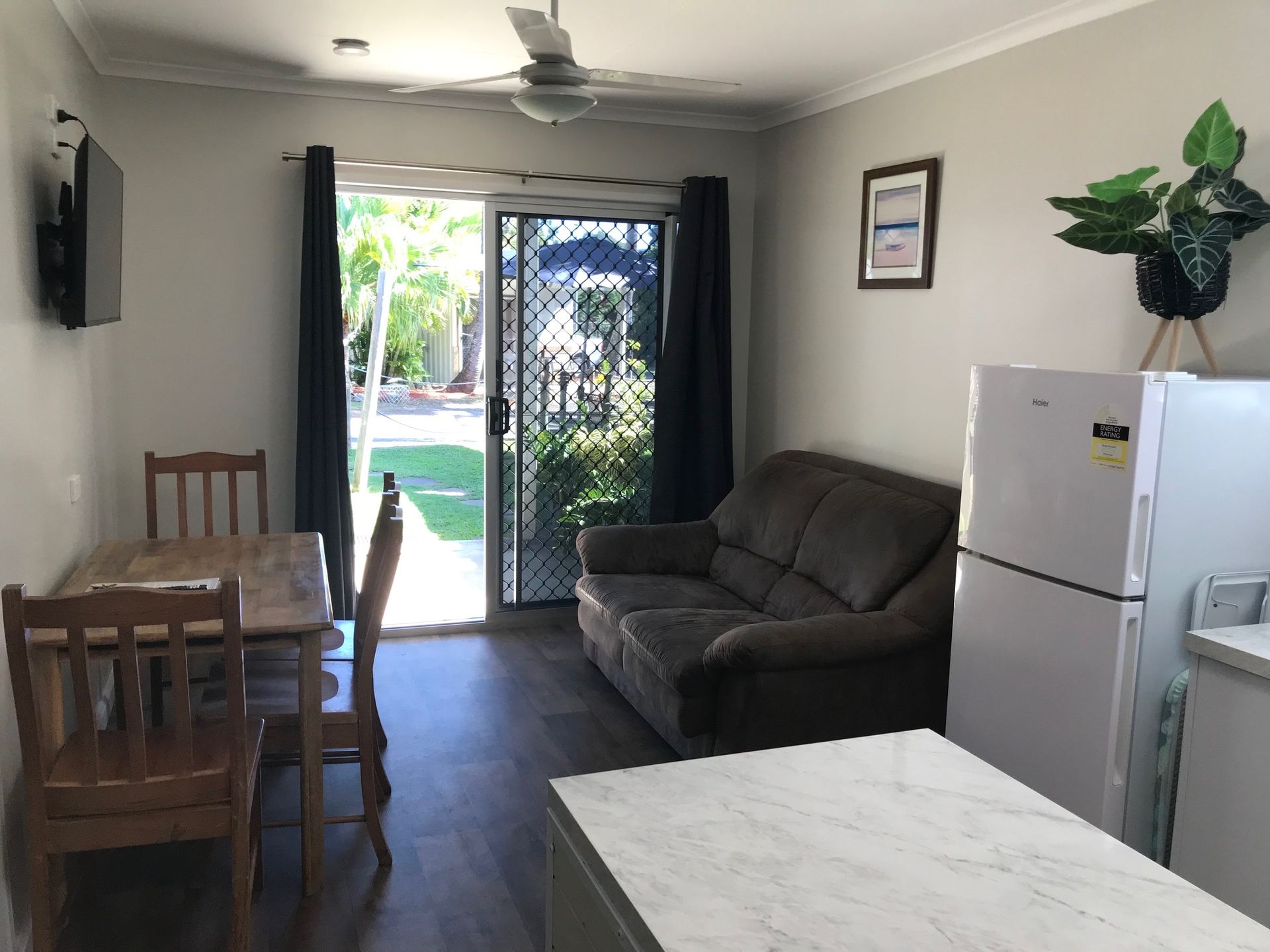 A Living Room With A Couch, Table And Chairs And A Refrigerator — Bush Village Holiday Cabins In Cannonvale, QLD