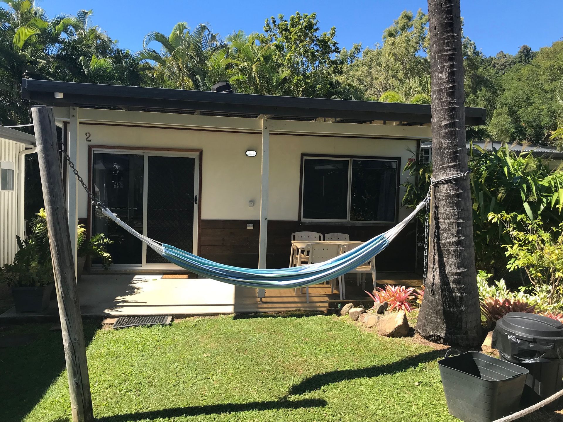 A Hammock Is Hanging In Front Of A Small House — Bush Village Holiday Cabins In Cannonvale, QLD