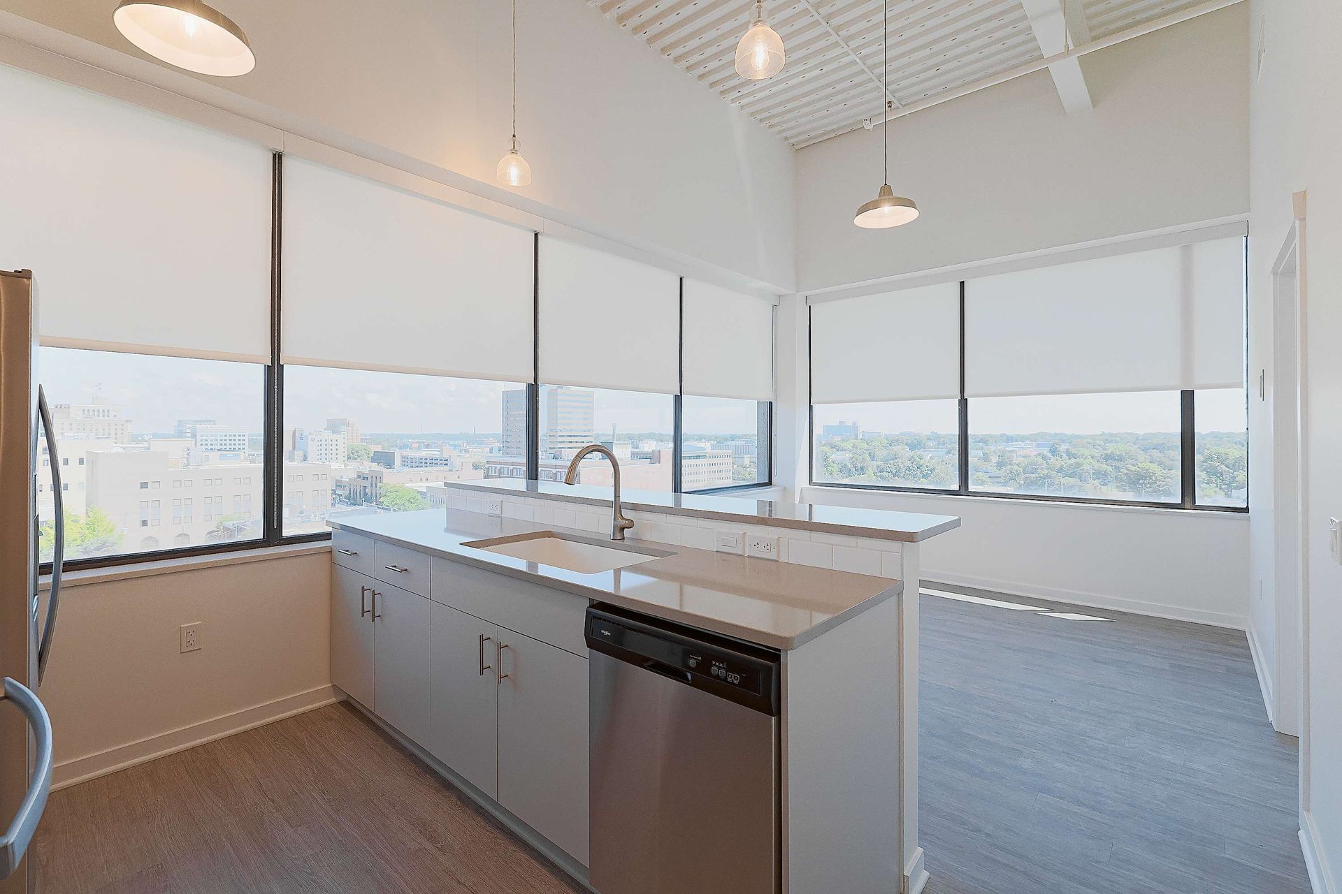 An empty kitchen with a sink , dishwasher , refrigerator and large windows.