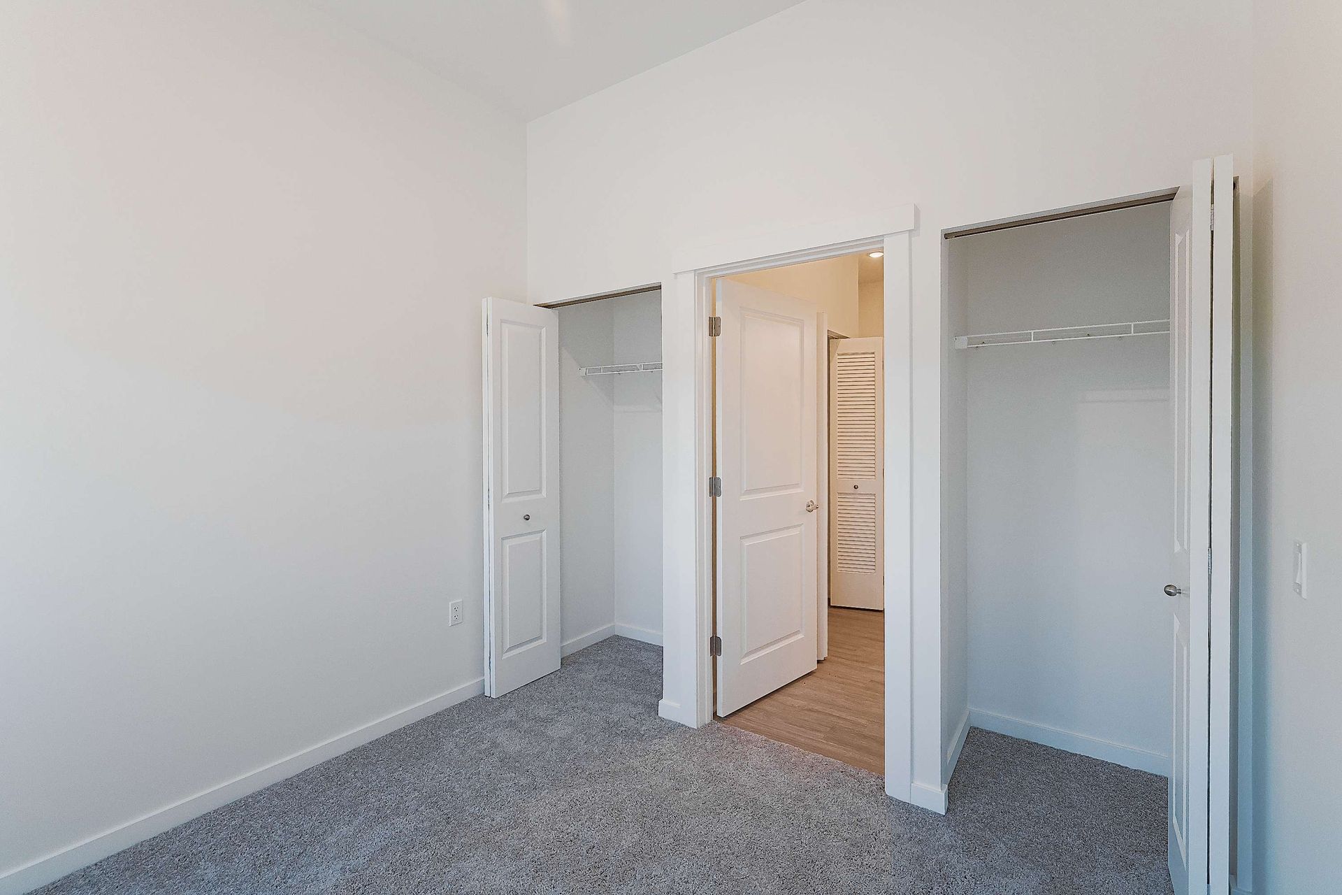 An empty bedroom with two closets and a carpeted floor.