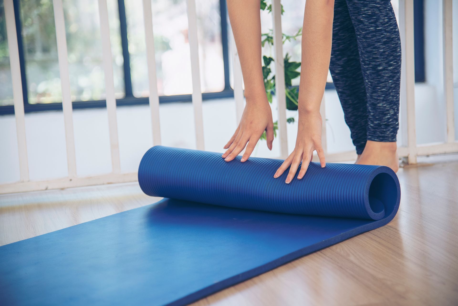 A woman is rolling a blue yoga mat on the floor.