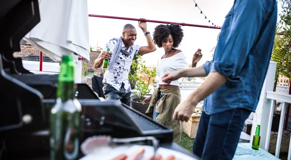 A group of people are dancing around a grill at a party.