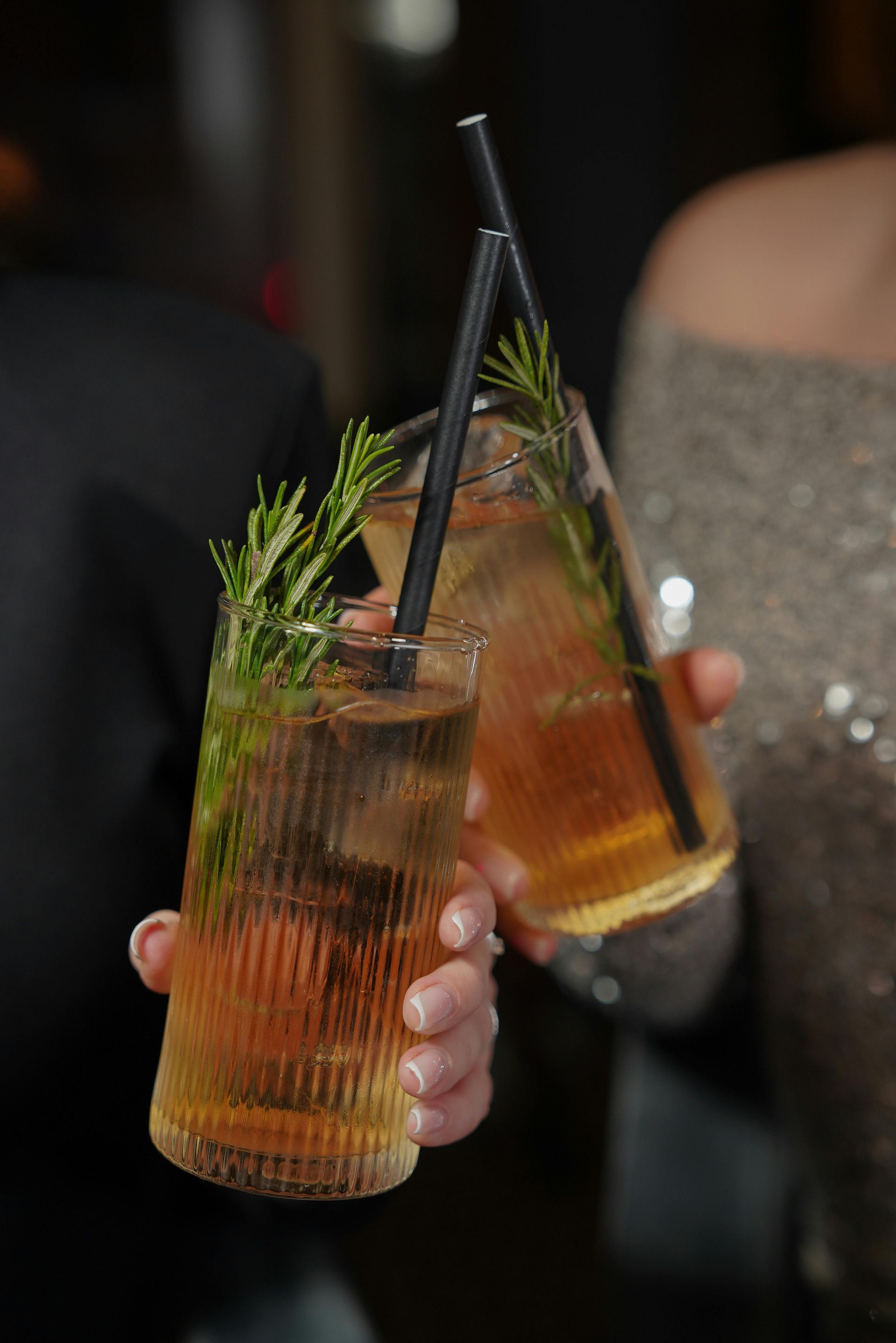 A woman is holding two drinks with straws in her hands.