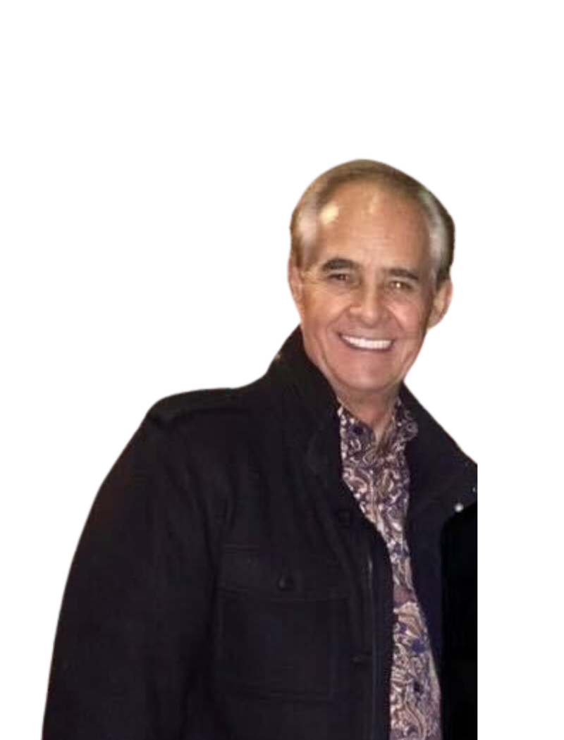 Smiling older man in a black jacket and patterned shirt, against a white background.