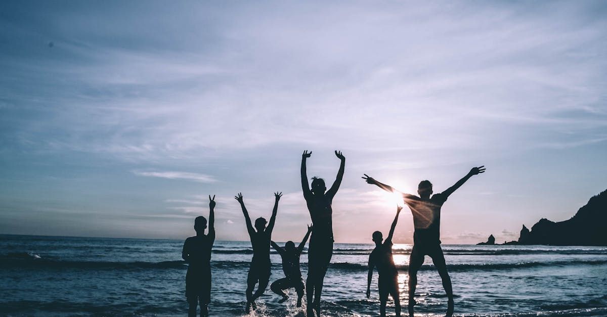 Silhouetted people jumping joyfully on a beach at sunset, arms raised.