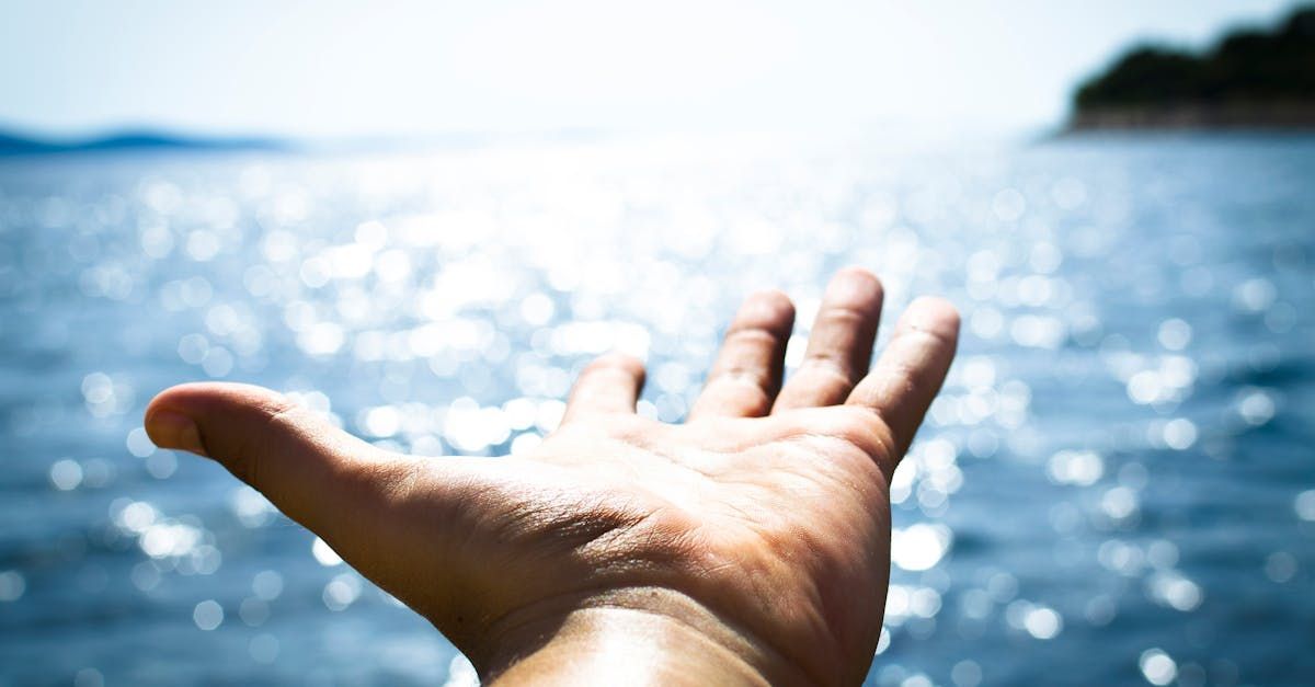 Hand reaching toward shimmering blue ocean.
