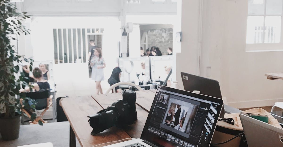 A woman in a white dress walks through a bright office. A laptop and camera sit on a wooden desk.