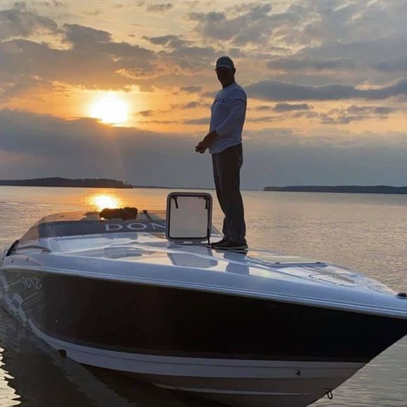 A man is standing on top of a boat in the water at sunset