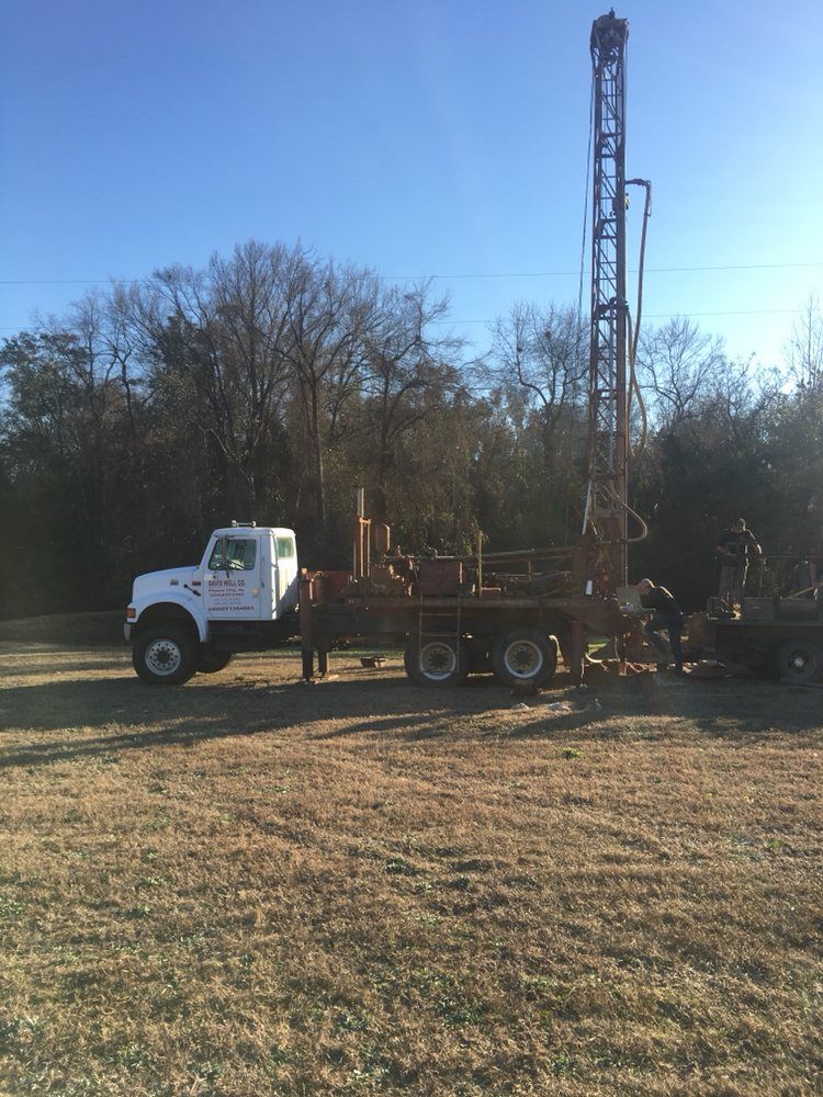 White drilling rig truck in a field drilling a well.