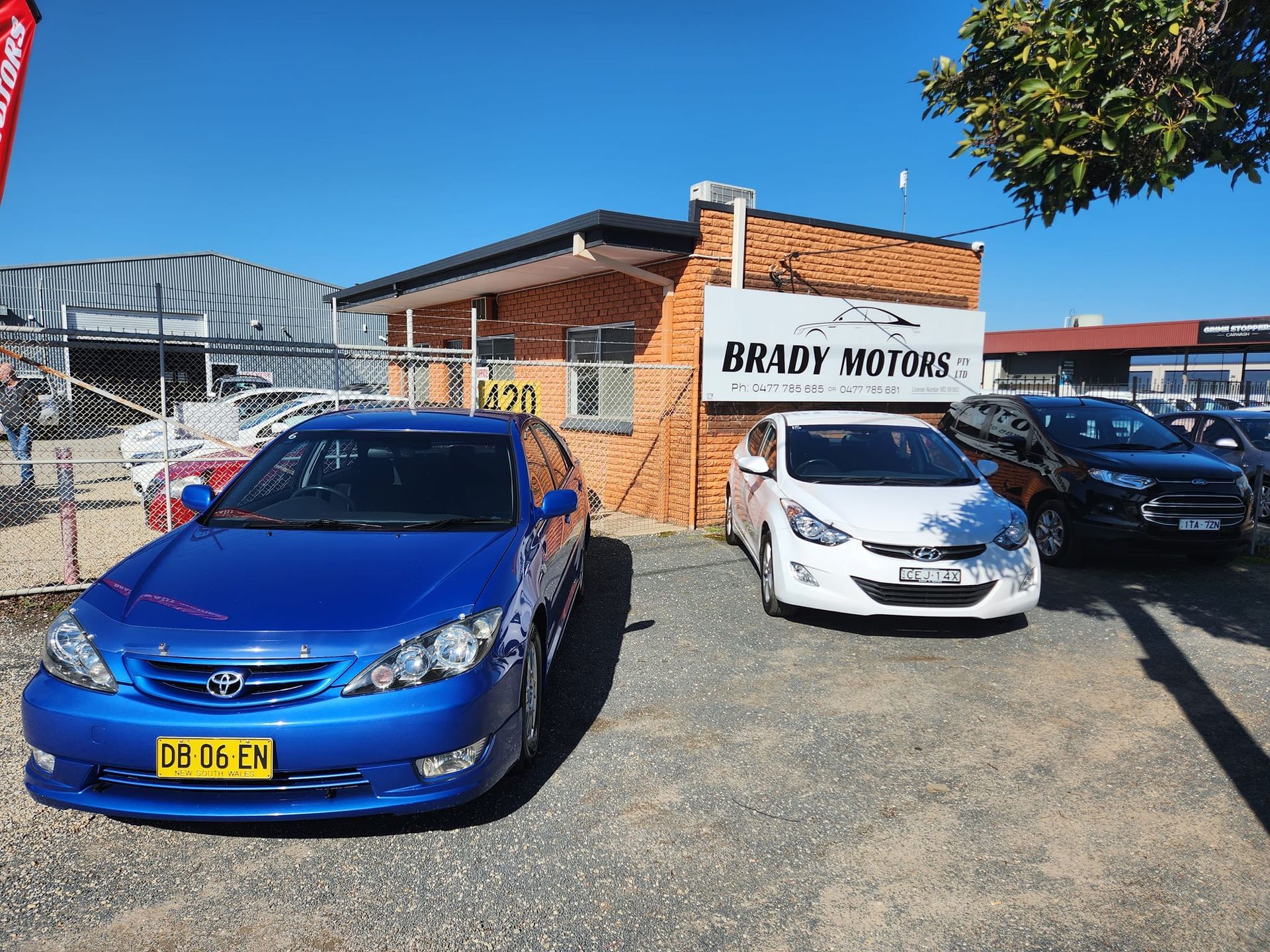 Cars parked in front of a car dealership, Brady Motors. A blue Toyota is prominent in the foreground.