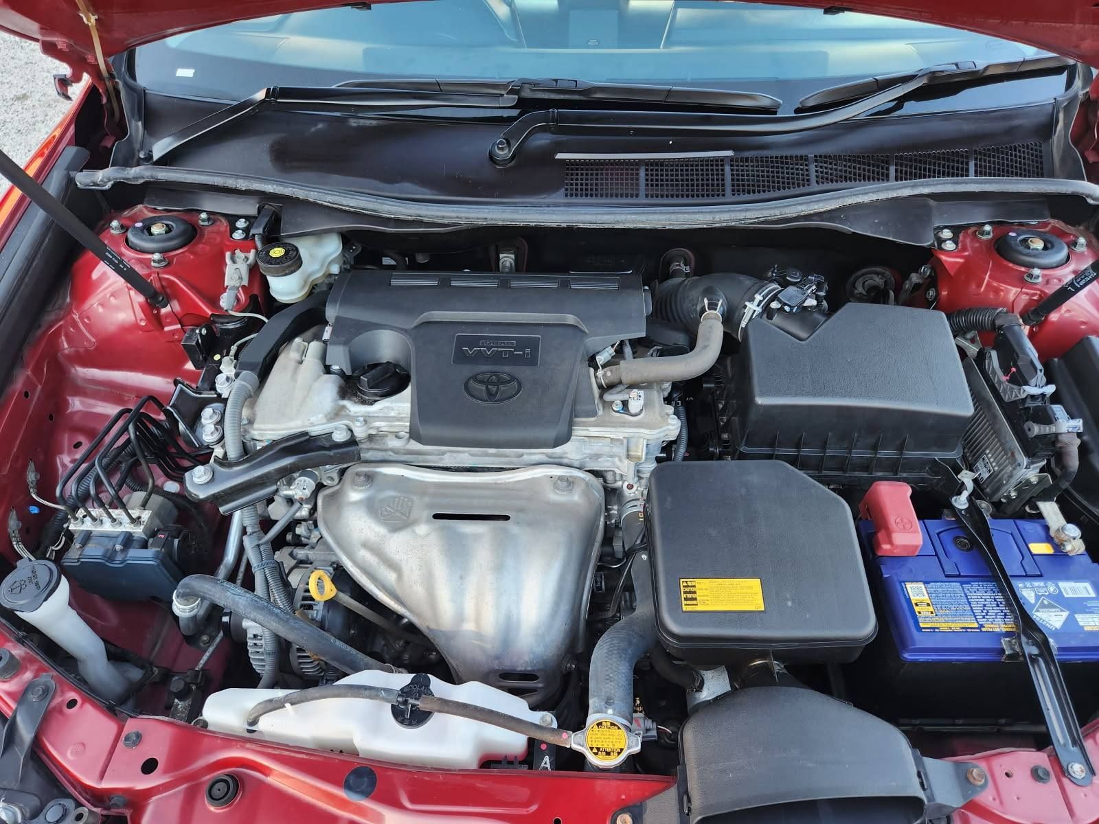 Red car engine bay with a Toyota engine visible, including various components and a blue battery.