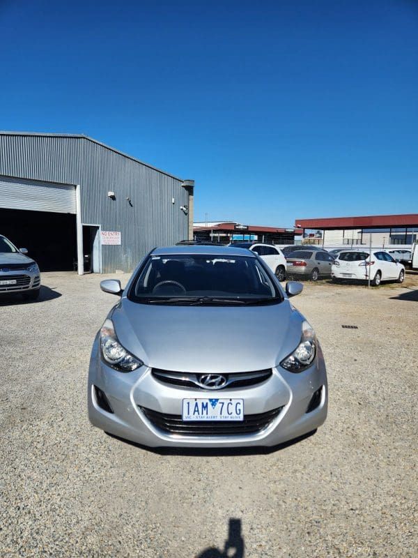 A silver Hyundai Elantra parked in front of a building, with a blue sky overhead.